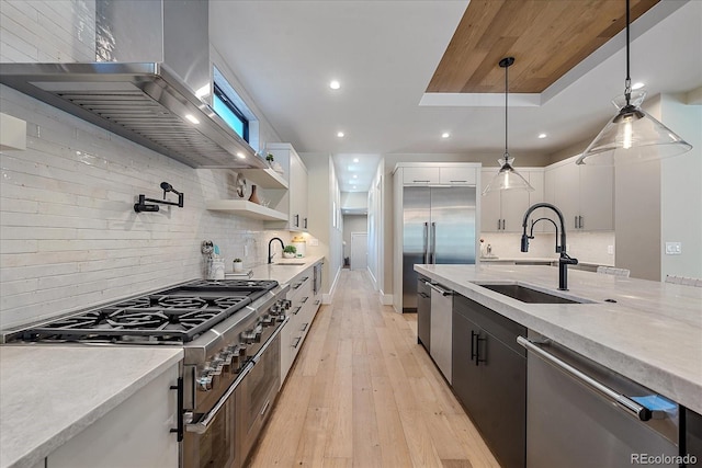 kitchen featuring premium appliances, white cabinets, decorative light fixtures, sink, and wall chimney exhaust hood