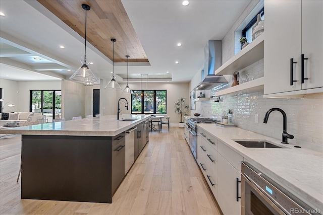 kitchen with white cabinetry, sink, decorative light fixtures, an island with sink, and wall chimney exhaust hood