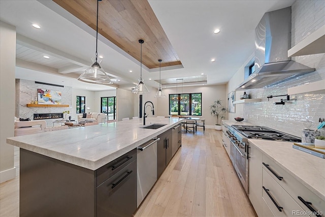 kitchen featuring a spacious island, white cabinetry, hanging light fixtures, stainless steel dishwasher, and wall chimney exhaust hood