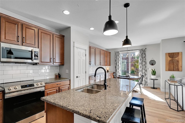 kitchen with sink, hanging light fixtures, light stone counters, stainless steel appliances, and a center island with sink