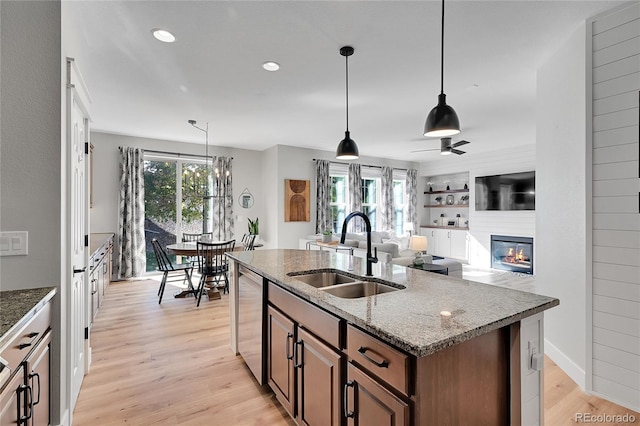 kitchen with sink, decorative light fixtures, stainless steel dishwasher, light stone countertops, and a kitchen island with sink