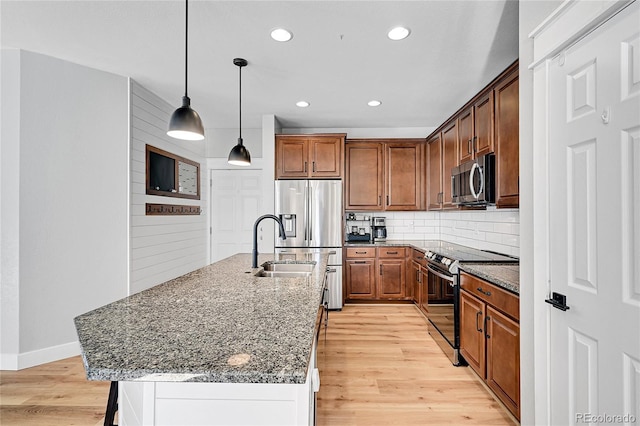 kitchen featuring appliances with stainless steel finishes, an island with sink, decorative backsplash, decorative light fixtures, and light wood-type flooring