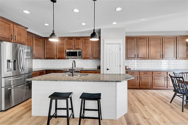 kitchen with appliances with stainless steel finishes, sink, a kitchen island with sink, and hanging light fixtures