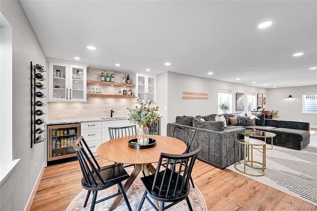 dining space with indoor wet bar, beverage cooler, and light wood-type flooring