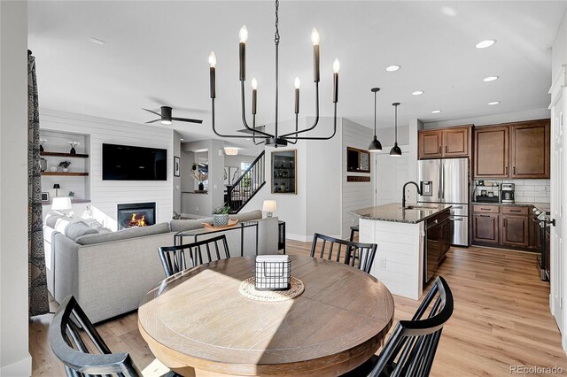 dining space featuring ceiling fan, a large fireplace, sink, and light wood-type flooring