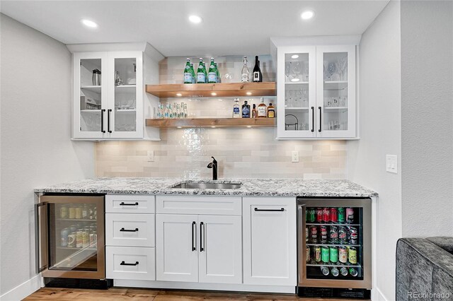 bar featuring light stone counters, beverage cooler, sink, and white cabinets