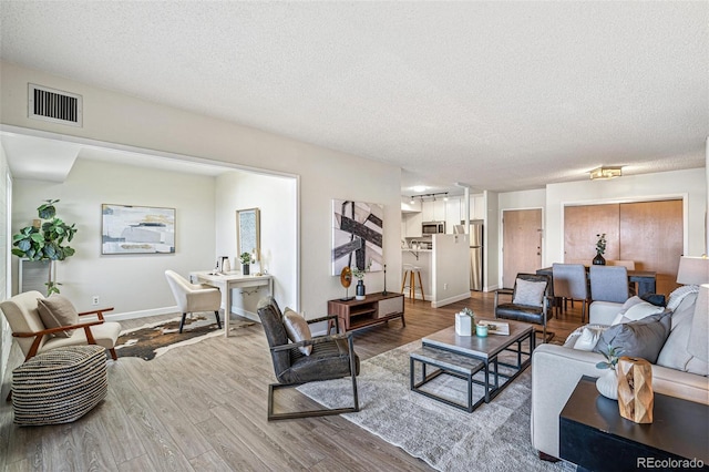 living area with visible vents, a textured ceiling, baseboards, and wood finished floors