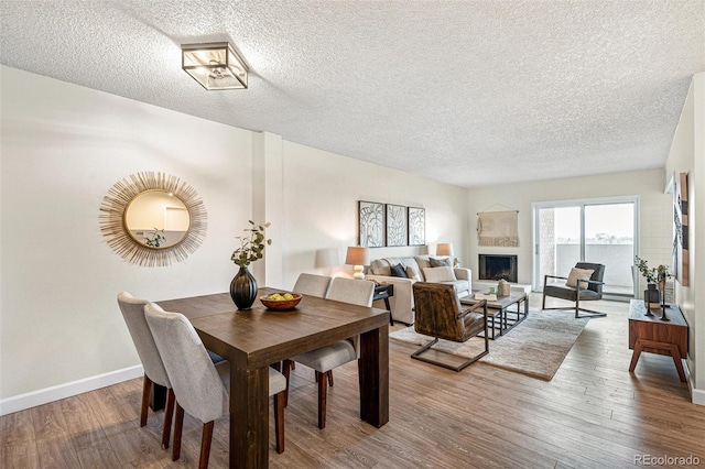 dining area featuring a fireplace, a textured ceiling, baseboards, and wood finished floors