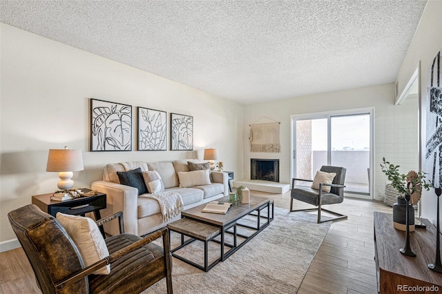 living room with a fireplace with raised hearth, a textured ceiling, and wood finished floors