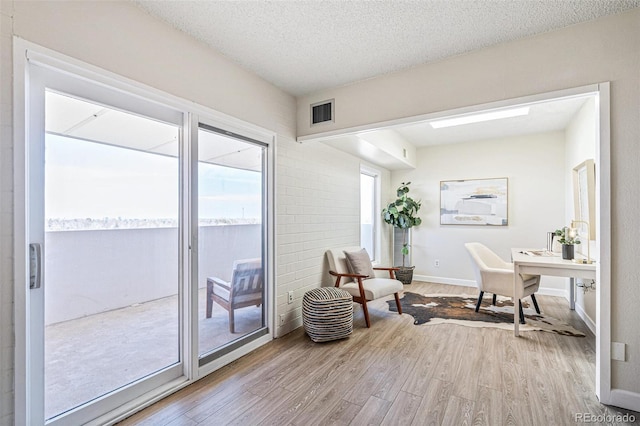 living area featuring visible vents, a textured ceiling, baseboards, and wood finished floors