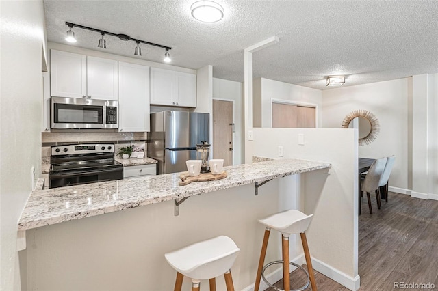 kitchen with a peninsula, appliances with stainless steel finishes, dark wood-style flooring, and light stone counters