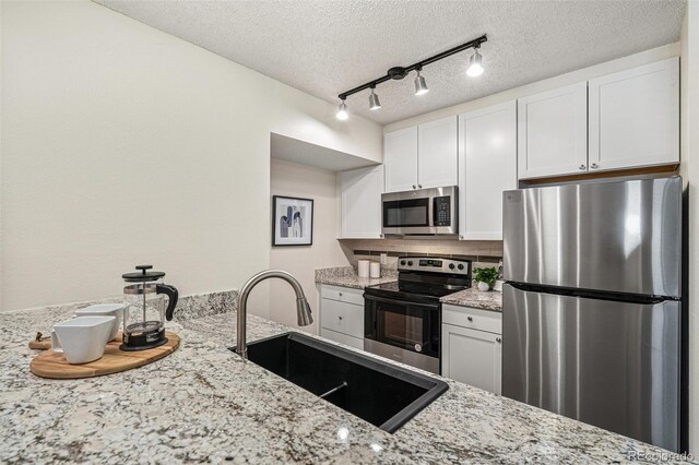 kitchen featuring a textured ceiling, white cabinetry, stainless steel appliances, and a sink