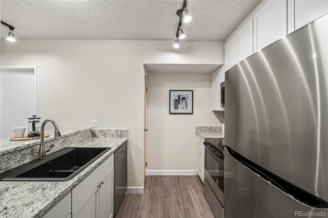 kitchen with a textured ceiling, stainless steel appliances, wood finished floors, a sink, and white cabinetry