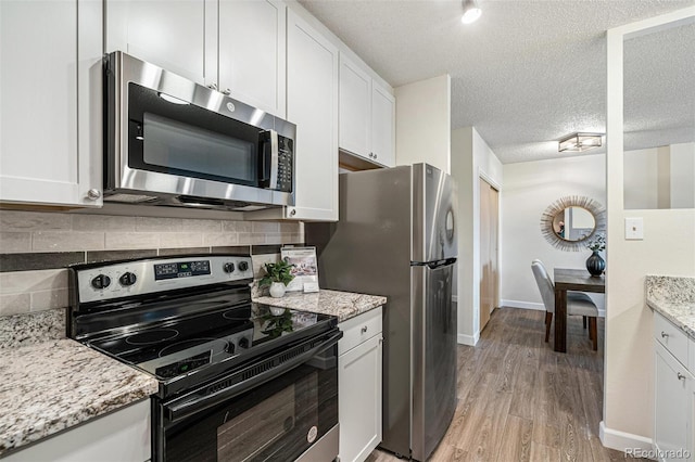 kitchen with tasteful backsplash, appliances with stainless steel finishes, light wood-style floors, white cabinets, and a textured ceiling