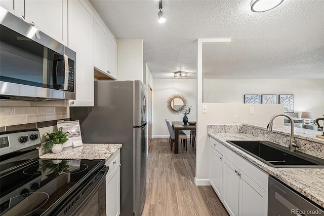 kitchen with a sink, white cabinets, appliances with stainless steel finishes, light wood-type flooring, and decorative backsplash