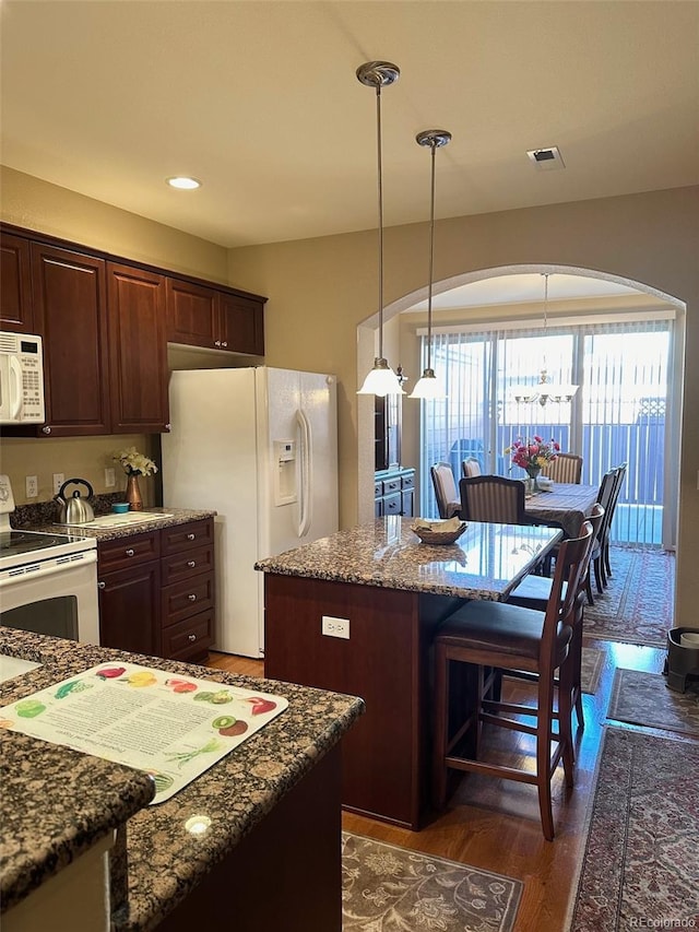 kitchen with white appliances, a kitchen island, dark hardwood / wood-style flooring, dark brown cabinetry, and dark stone countertops