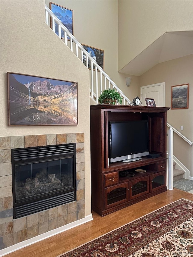 unfurnished living room with vaulted ceiling, a tiled fireplace, and wood-type flooring