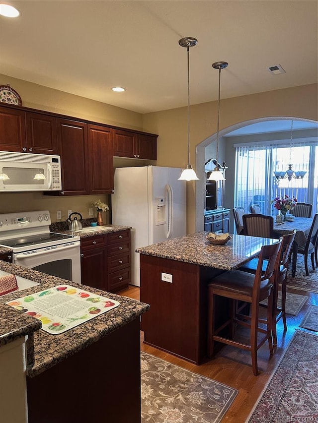 kitchen featuring white appliances, dark brown cabinets, a center island, dark hardwood / wood-style flooring, and decorative light fixtures