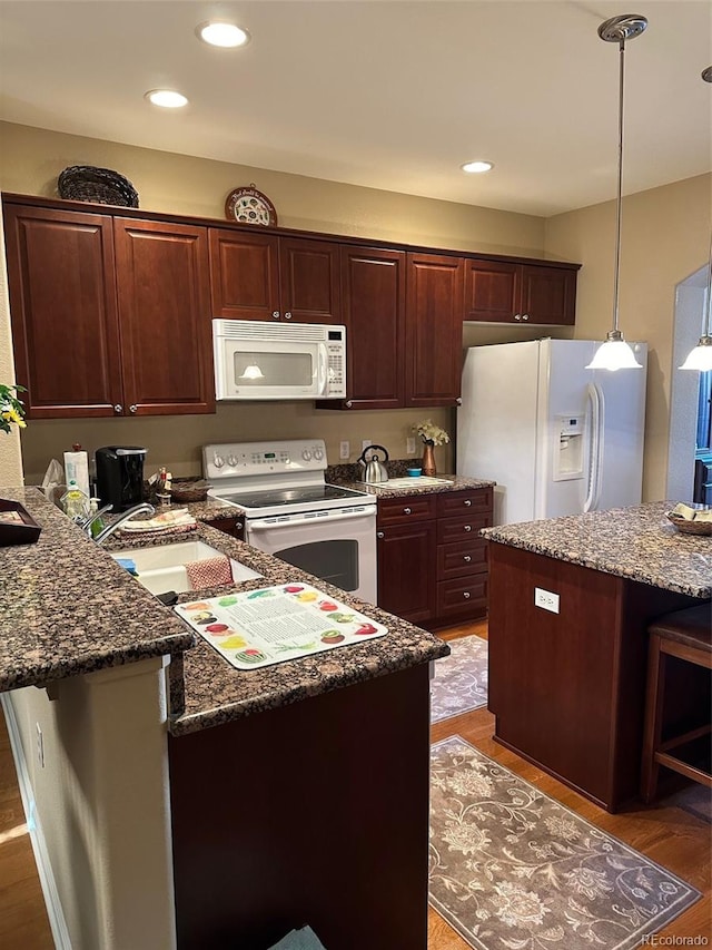 kitchen with dark stone countertops, decorative light fixtures, dark wood-type flooring, and white appliances