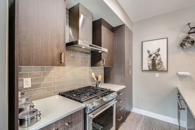 kitchen featuring dark brown cabinetry, light wood-type flooring, stainless steel stove, decorative backsplash, and wall chimney range hood