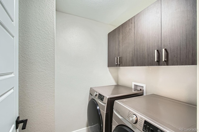 washroom featuring washer and dryer, cabinet space, and a textured wall