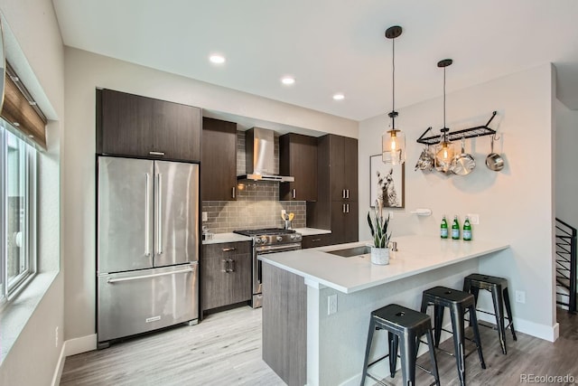 kitchen featuring dark brown cabinetry, appliances with stainless steel finishes, wall chimney exhaust hood, and a kitchen breakfast bar