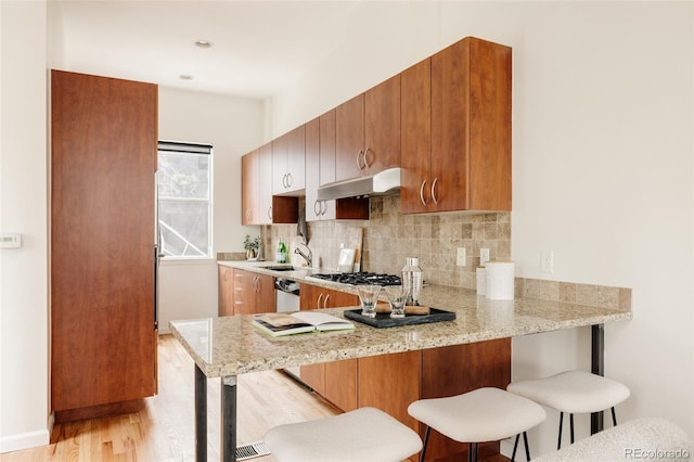 2680 Blake St Unit 12, Denver, CO 80205 - kitchen with under cabinet range hood, a kitchen bar, decorative backsplash, light wood finished floors, and a peninsula
