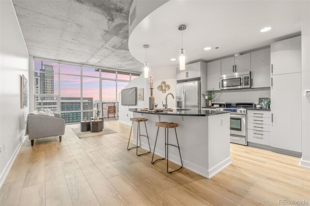 kitchen featuring stainless steel appliances, pendant lighting, light wood finished floors, and a breakfast bar area