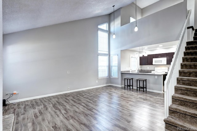 unfurnished living room with light wood-type flooring, a wealth of natural light, a textured ceiling, and a high ceiling