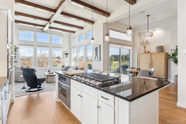 kitchen featuring open floor plan, white cabinetry, stainless steel appliances, light wood-style floors, and beamed ceiling