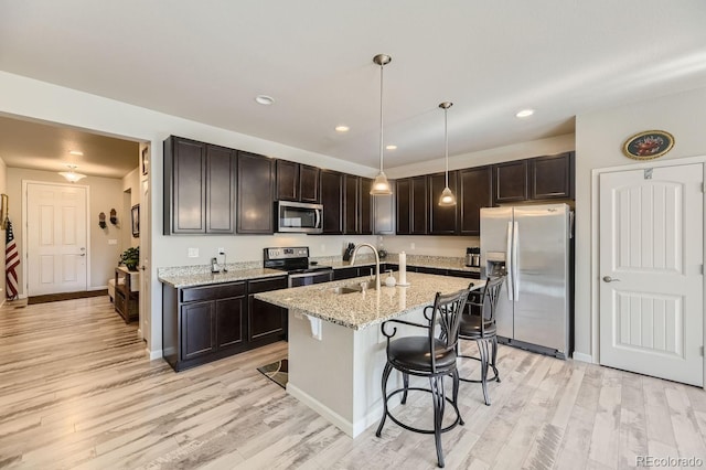 kitchen featuring stainless steel appliances, decorative light fixtures, dark brown cabinets, light hardwood / wood-style floors, and a breakfast bar area