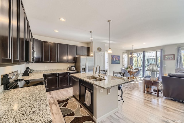 kitchen featuring stainless steel appliances, light hardwood / wood-style floors, sink, a breakfast bar, and pendant lighting