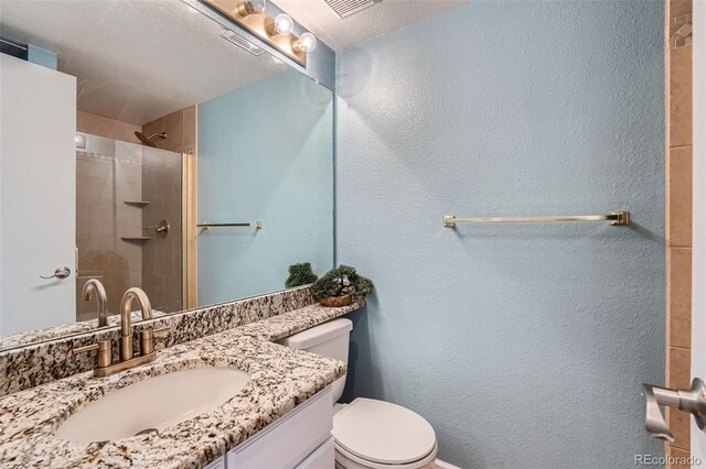 bathroom featuring vanity, toilet, a textured ceiling, and tiled shower