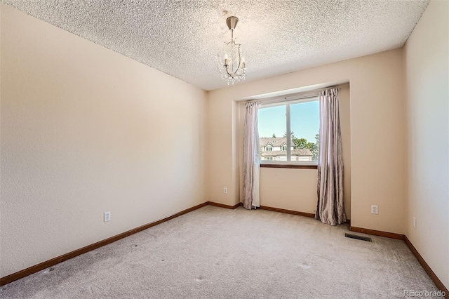 carpeted empty room featuring a notable chandelier and a textured ceiling