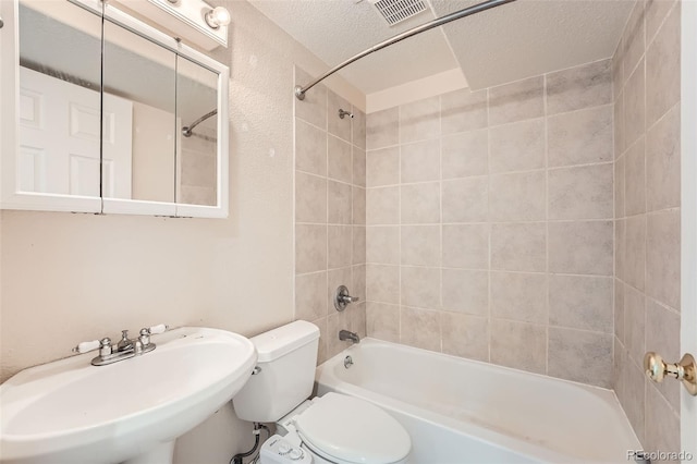 full bathroom with toilet, tiled shower / bath, a textured ceiling, and sink