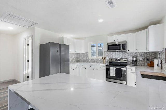 kitchen with white cabinets, light stone counters, appliances with stainless steel finishes, and tasteful backsplash