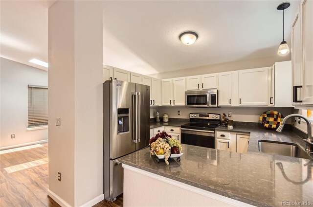 8432 S Upham Way, Littleton, CO 80128 - kitchen with appliances with stainless steel finishes, wood finished floors, dark stone counters, a peninsula, and pendant lighting