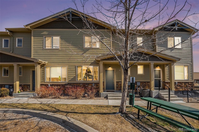 back of property featuring stone siding and covered porch