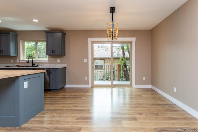 kitchen with pendant lighting, stainless steel dishwasher, sink, and light hardwood / wood-style floors