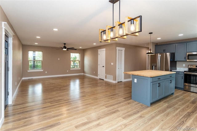 kitchen featuring light wood-type flooring, pendant lighting, wooden counters, a kitchen island, and appliances with stainless steel finishes