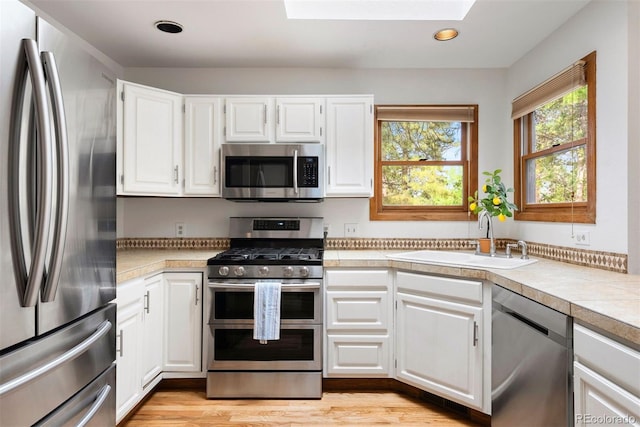 23599 Shingle Creek Rd, Golden, CO 80401 - kitchen with stainless steel appliances, light countertops, a skylight, white cabinetry, and recessed lighting