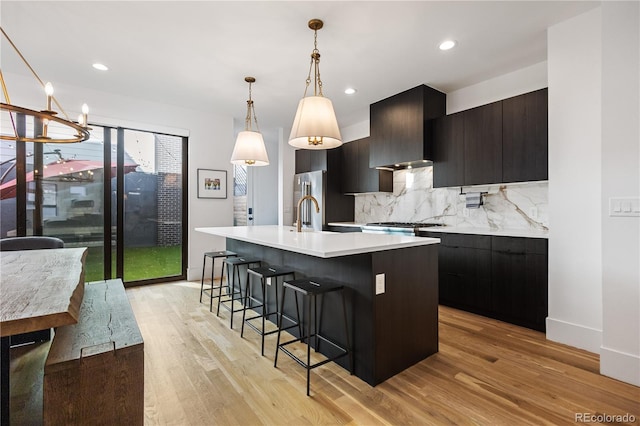 2625 W 23rd Ave, Denver, CO 80211 - kitchen featuring tasteful backsplash, a kitchen island with sink, light wood-type flooring, a breakfast bar area, and light countertops