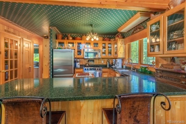 kitchen with a notable chandelier, crown molding, appliances with stainless steel finishes, wooden walls, and sink