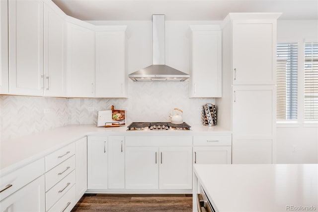 kitchen featuring wall chimney range hood, dark wood-type flooring, white cabinetry, backsplash, and stainless steel gas cooktop