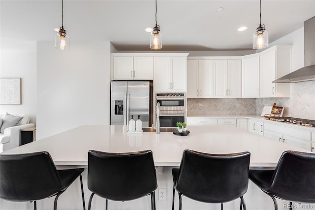 kitchen featuring white cabinetry, hanging light fixtures, stainless steel appliances, and a center island with sink