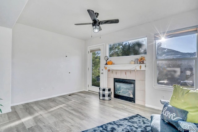 living room featuring ceiling fan, a tile fireplace, and light hardwood / wood-style flooring