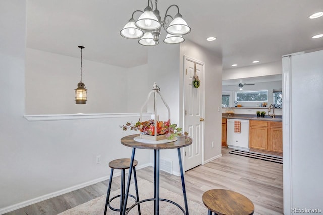 kitchen featuring dishwasher, ceiling fan with notable chandelier, hanging light fixtures, sink, and light hardwood / wood-style flooring