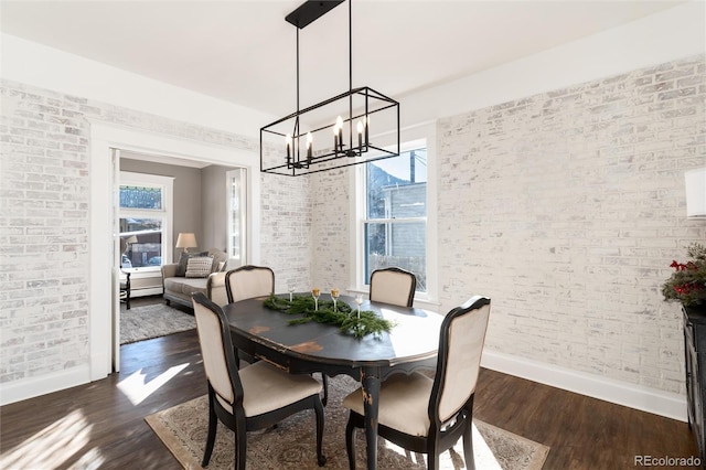 dining space with brick wall, dark hardwood / wood-style floors, and an inviting chandelier