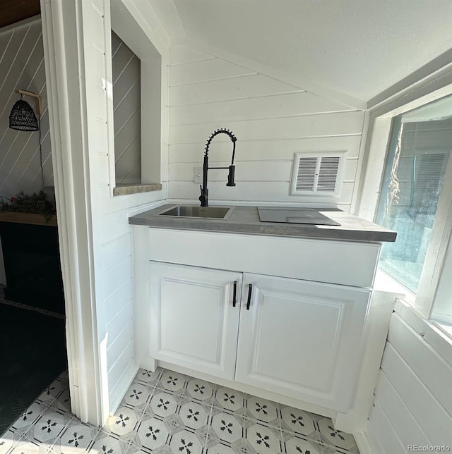 interior space featuring vaulted ceiling, sink, white cabinets, and wood walls