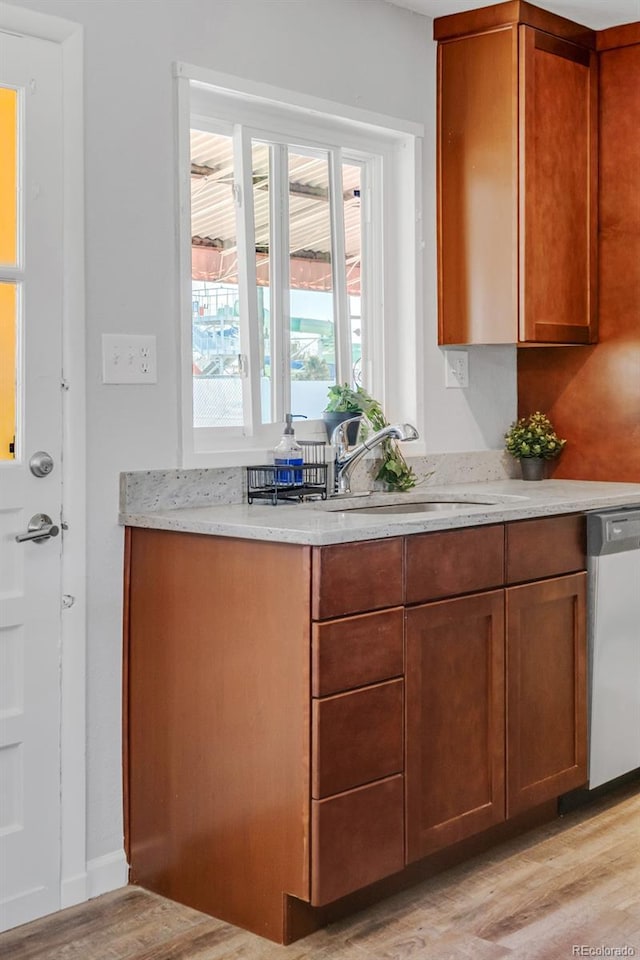 kitchen with sink, stainless steel dishwasher, light stone counters, and light wood-type flooring